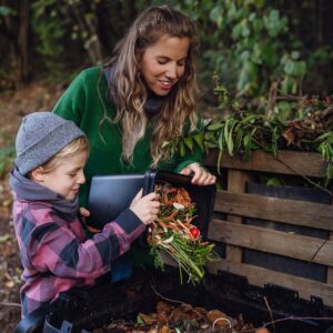 Boy helping mother to put kitchen waste, peel and leftover vegetables scraps into composter in the garden. Concept of composting kitchen biodegradable waste. jardinage compost